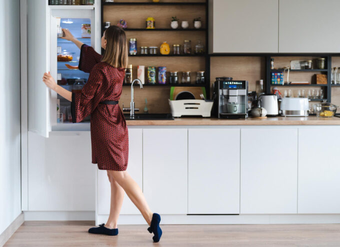 mujer-hambrienta-buscando-comida-nevera-casa-pero-no-tiene-mucho-alli-muebles-cocina-blancos-ropa-casa-tunica-seda-roja